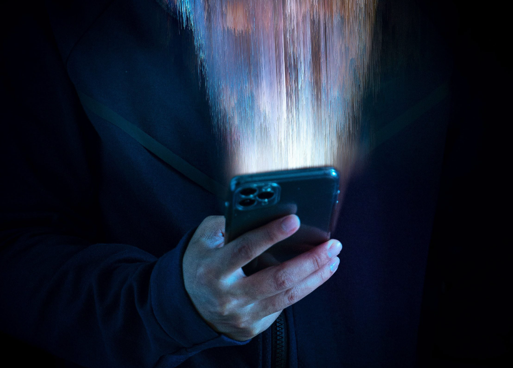 A person in dark clothes holding a cell phone in one hand, the phone is emitting artificial streams of light. 