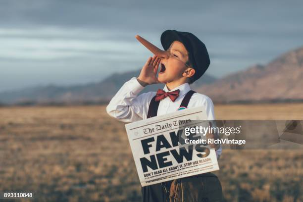 Child holding up a news paper that reads FAKE NEWS. Child is also wearing a Pinocchio nose.