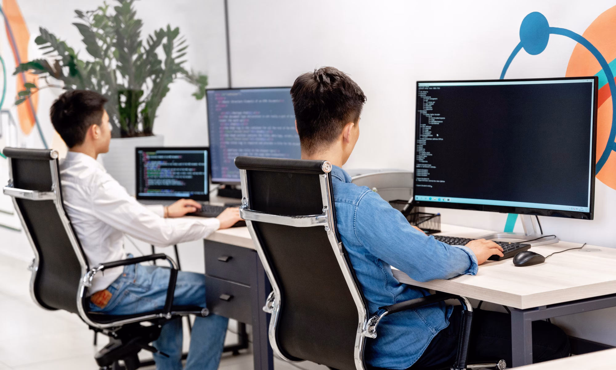 Two people working at separate desks on computers with code displayed on their screens.